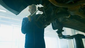 Mechanic in blue coverall fixing a vehicle in a well-lit auto workshop.